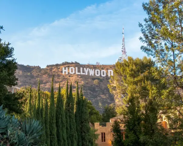 Il cartello "HOLLYWOOD" domina la collina, indicando dove si trova Hollywood, con alberi verdi e un cielo azzurro.