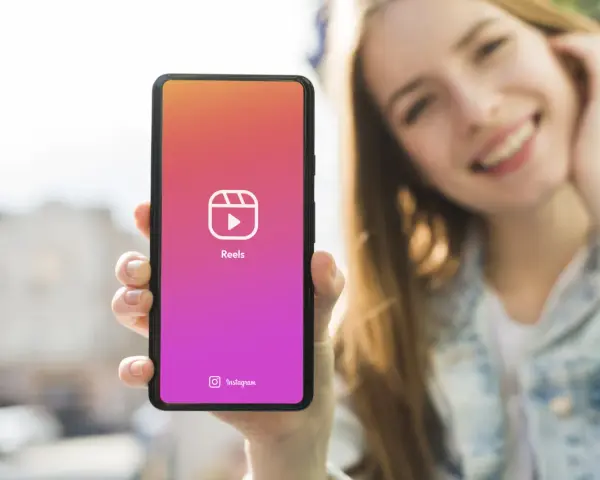 Una ragazza sorride mentre mostra il suo smartphone con l'icona di Reels, perfetta app per montare video e creare contenuti.