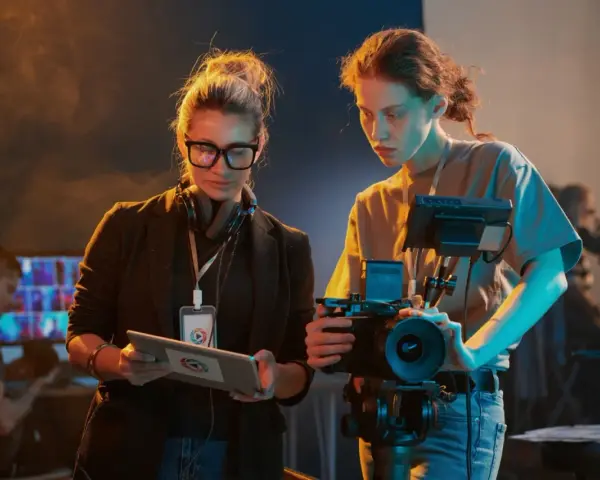 Due donne discutono le tecniche di ripresa, una con tablet, l'altra con videocamera.