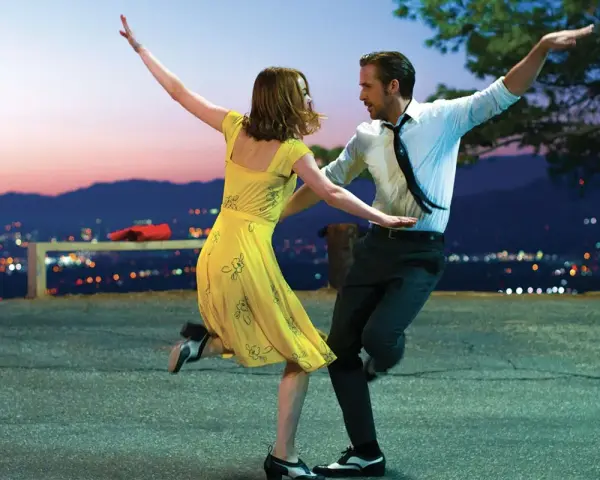 Coppia balla al tramonto, immersa nella musica diegetica che accompagna la loro danza, con la città illuminata sullo sfondo.