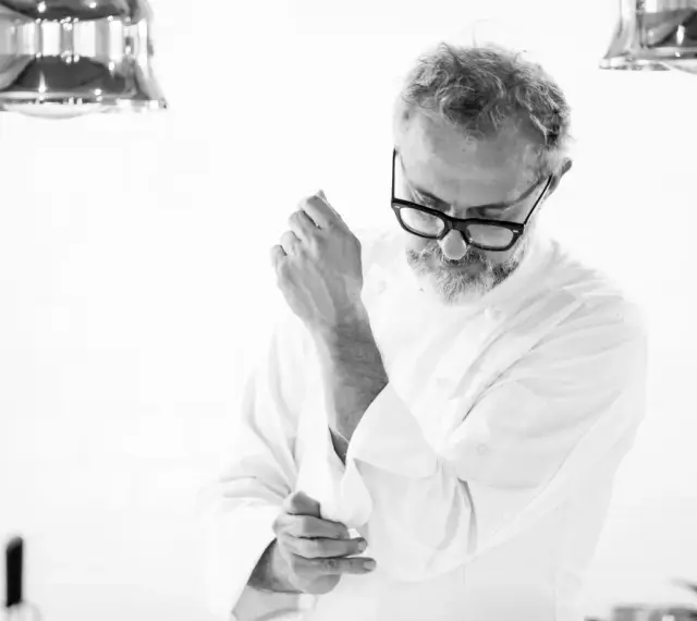 Julian works, aggiustandosi il polsino della giacca da chef. La sua espressione concentrata suggerisce la dedizione al suo mestiere.