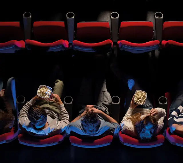 Persone sedute in un cinema, gustando popcorn, pronte per un film di Hollywood.