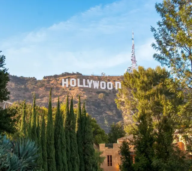 Il cartello "HOLLYWOOD" domina la collina, indicando dove si trova Hollywood, con alberi verdi e un cielo azzurro.