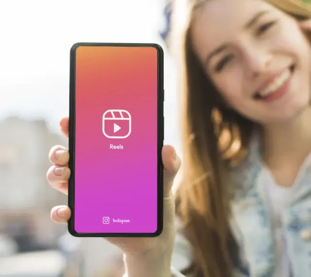 Una ragazza sorride mentre mostra il suo smartphone con l'icona di Reels, perfetta app per montare video e creare contenuti.
