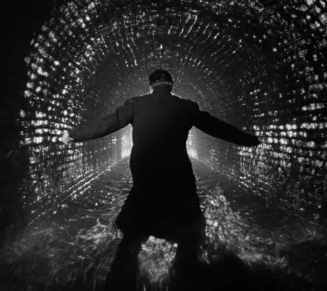 Uomo in un tunnel di mattoni illuminato, con le braccia aperte, come in un momento di rivelazione o un inaspettato plot twist.