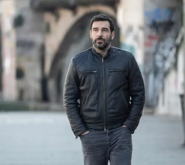 Edoardo Leo, con la sua aria pensierosa, cammina in un vicolo urbano, ricordando forse i suoi ruoli ne I Cesaroni.