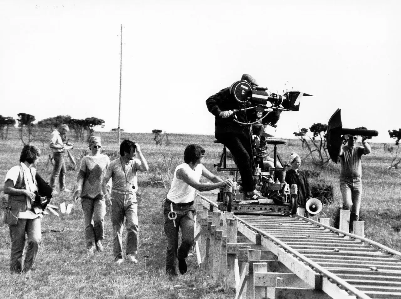 Crew sul set, con operatore alla macchina da presa su carrello e tecnico che maneggia un riflettore. Diverse tecniche di ripresa in azione.