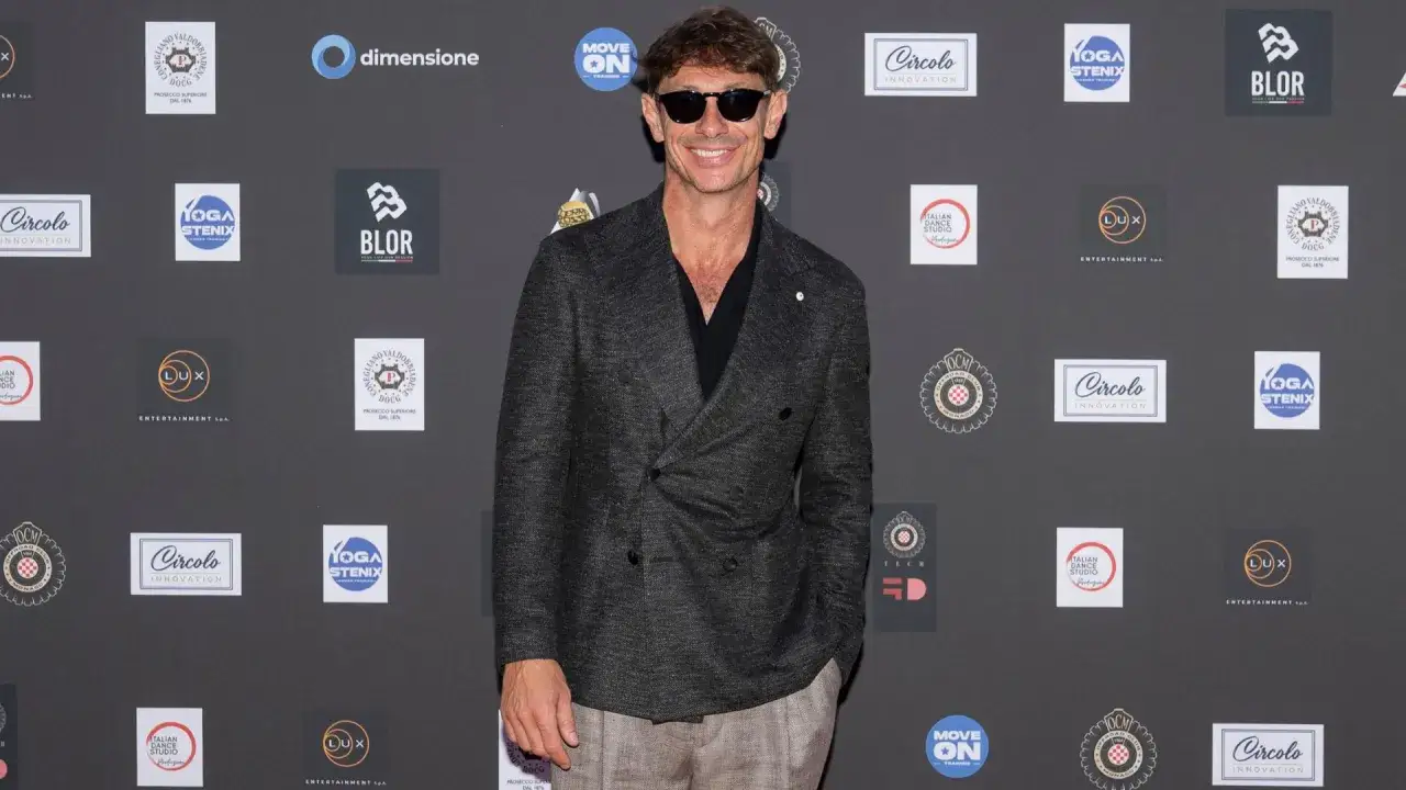 Giorgio Pasotti, sorridente e con occhiali da sole, posa davanti a uno sfondo di loghi. Le sue candidature per eventi futuri sembrano promettenti.