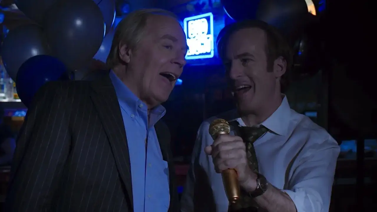 Due uomini cantano al karaoke, con palloncini e un neon 