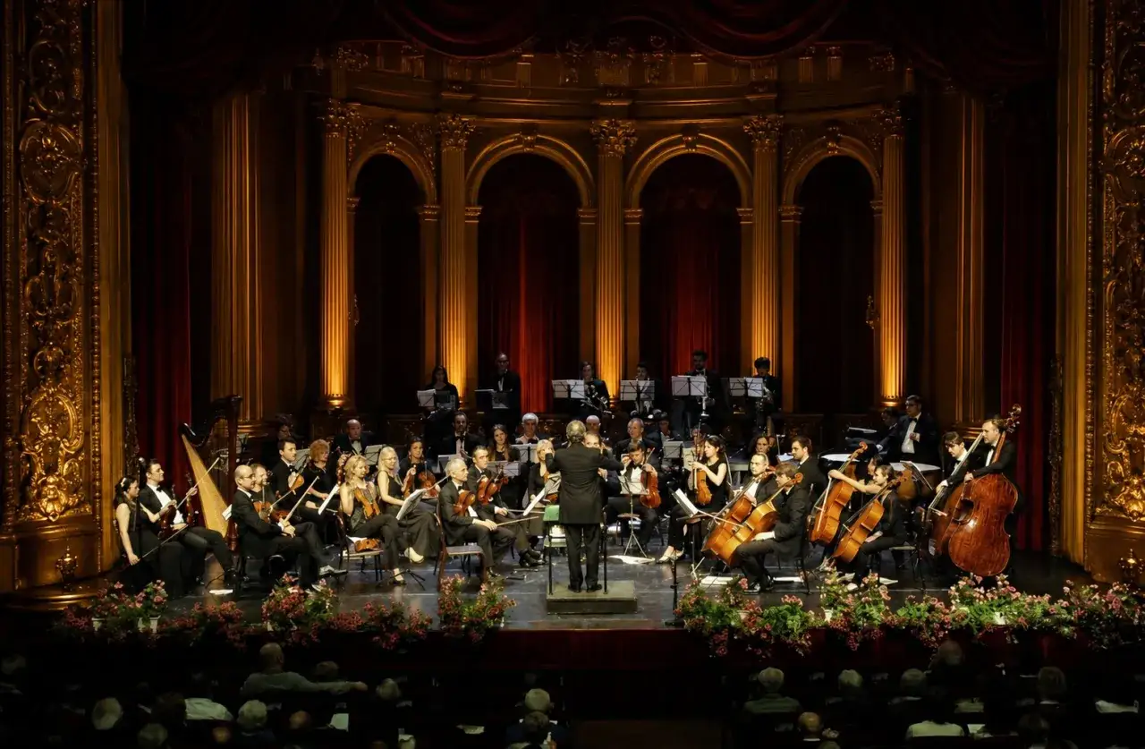 Concerto d'orchestra dal vivo, con musicisti che eseguono colonne sonore film italiani in un teatro sontuoso.