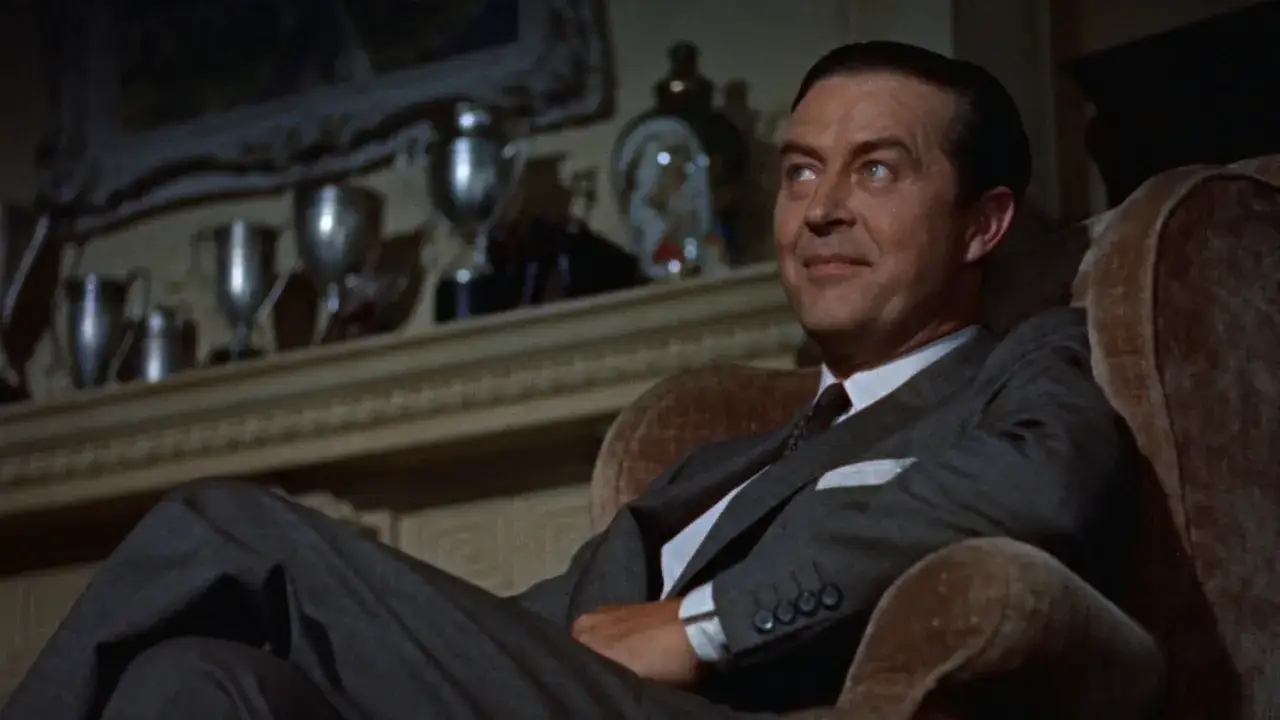 Un uomo elegante in poltrona, con trofei sullo sfondo, sembra meditare su il delitto perfetto spiegazione.