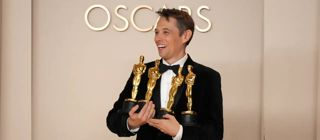 Simon Jacques, attore, sorride felice con quattro Oscar in mano.