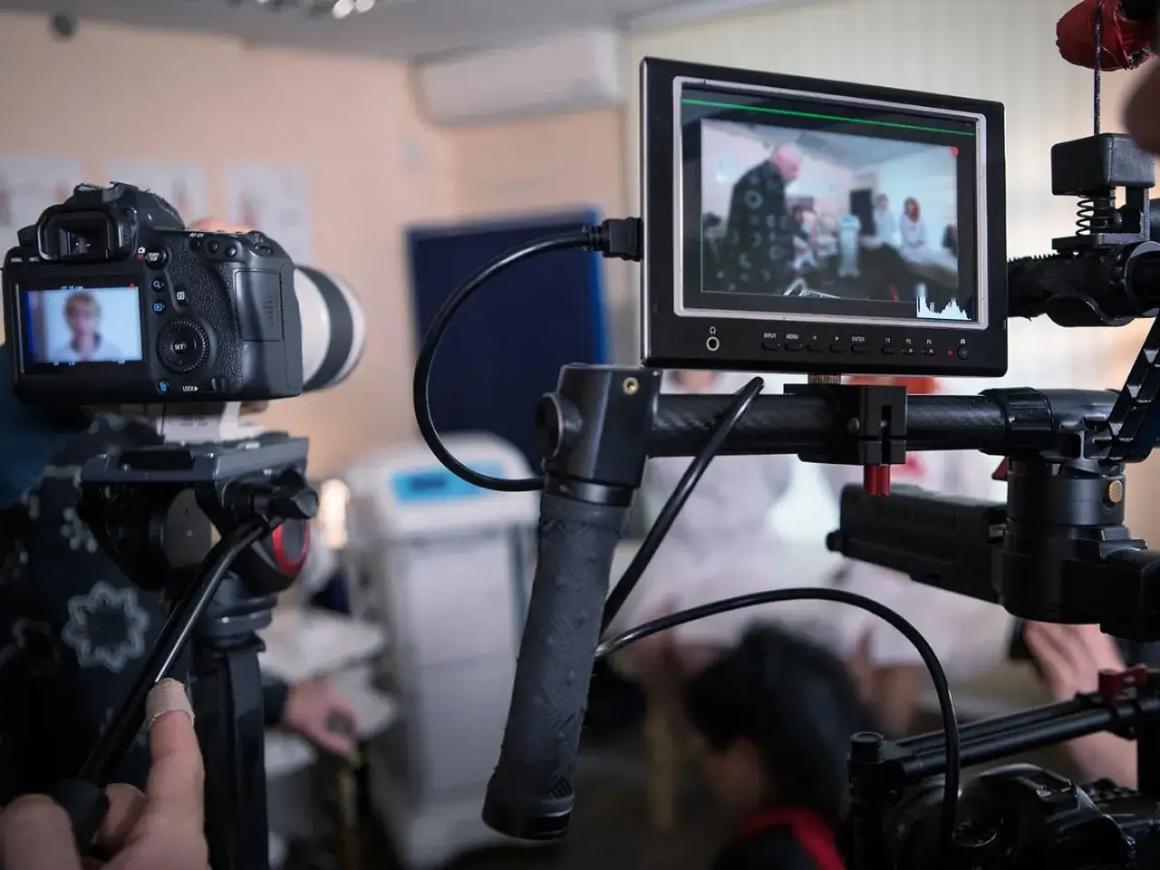 Attrezzatura per un film amatoriale: una telecamera su treppiede e un monitor che mostra una scena con persone.