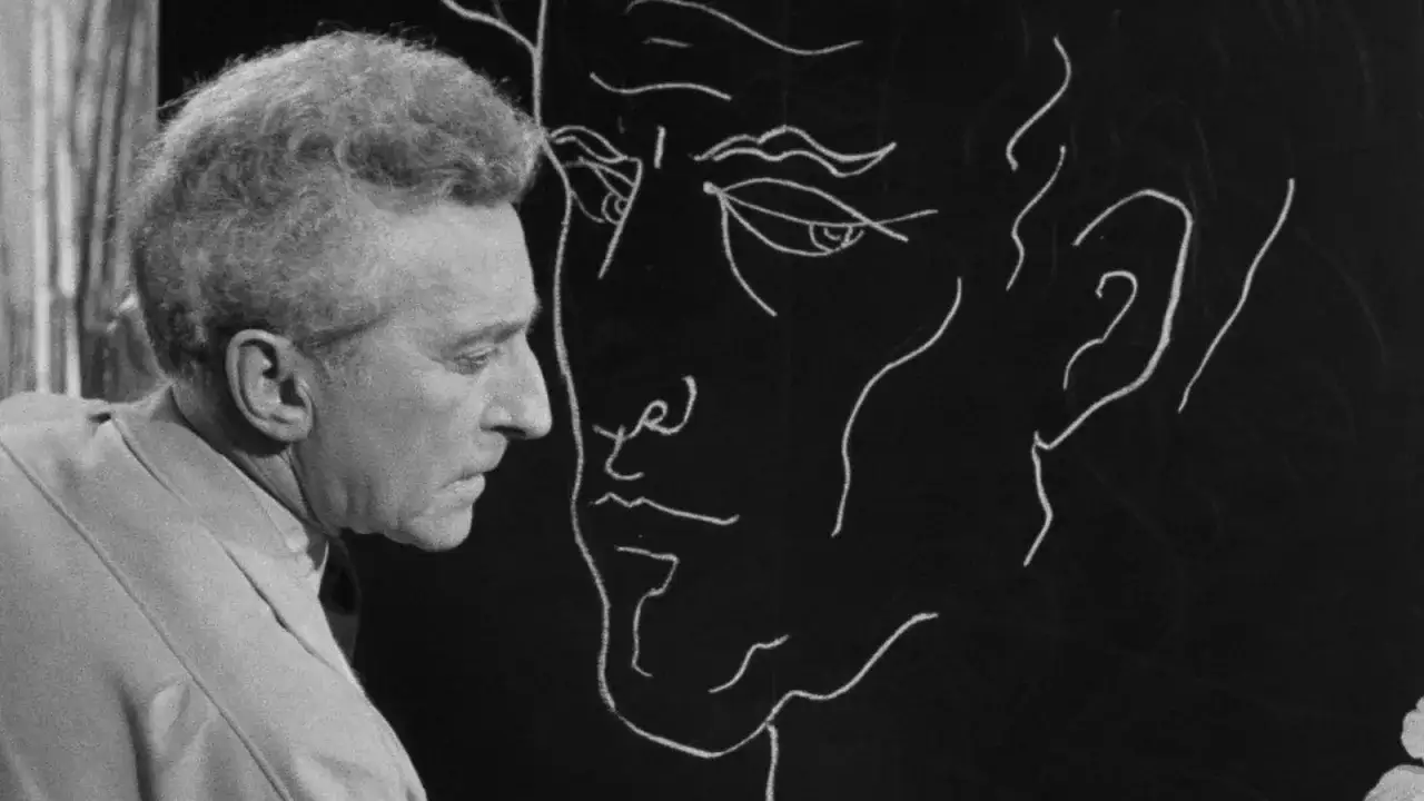 Un uomo guarda un disegno a gesso di un volto, un'immagine iconica dei film di Jean Cocteau.