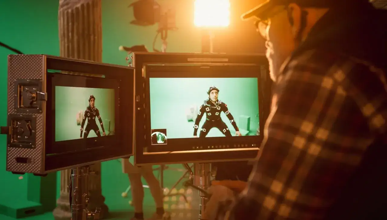 Dietro le quinte: un attore con tuta motion capture su green screen, monitor che mostrano la scena e un operatore. La magia degli effetti speciali cinema prende forma.
