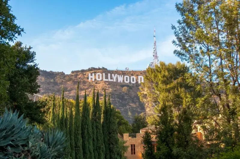 Il cartello "HOLLYWOOD" domina la collina, indicando dove si trova Hollywood, con alberi verdi e un cielo azzurro.
