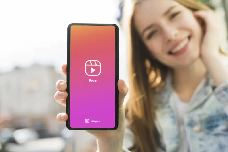 Una ragazza sorride mentre mostra il suo smartphone con l'icona di Reels, perfetta app per montare video e creare contenuti.
